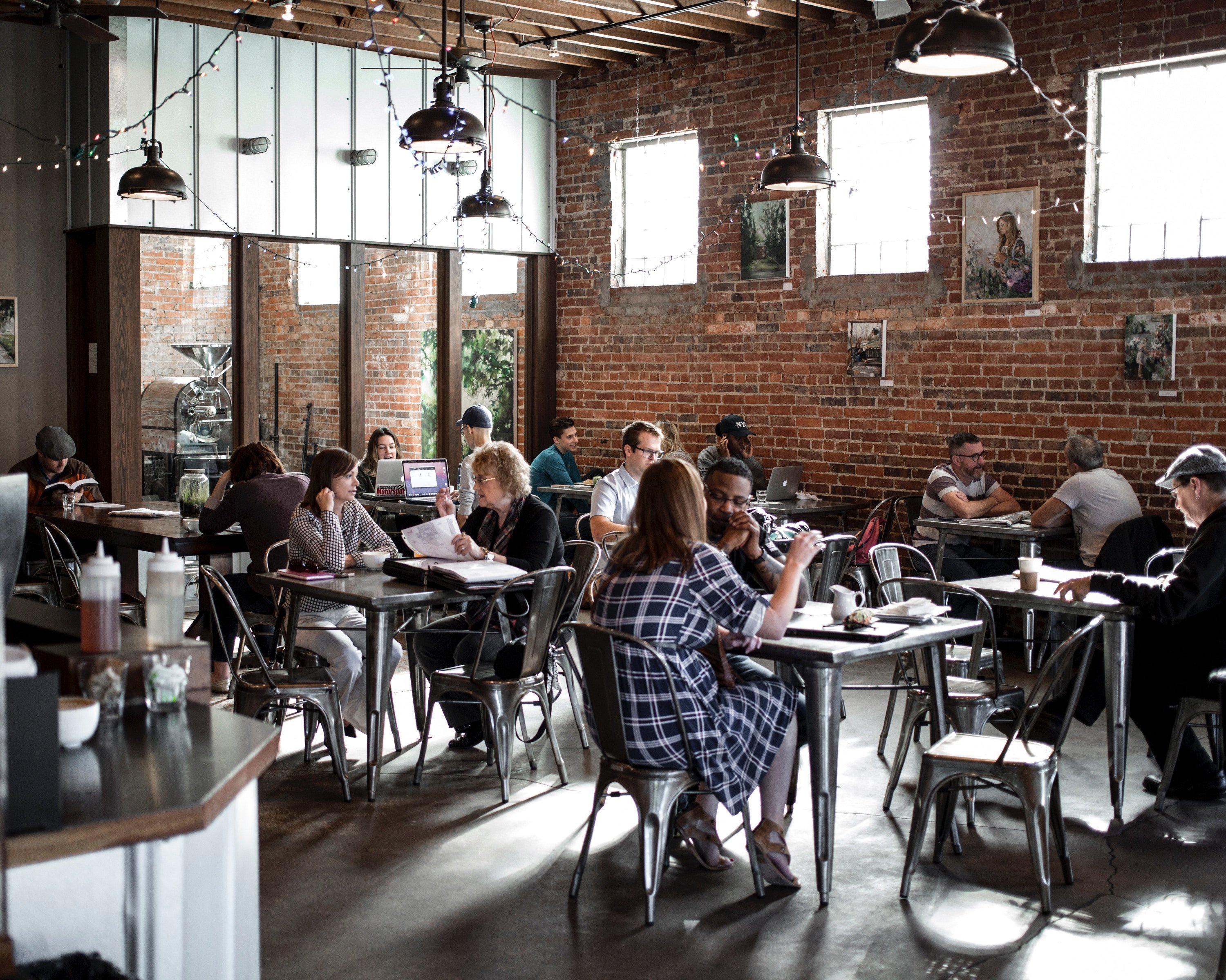 Casual-professional café full of people sitting at various tables, speaking together, while working, eating or reading