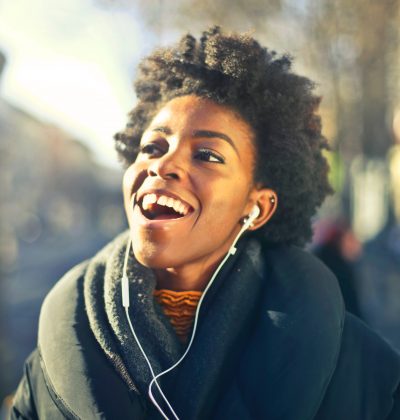Woman walking in a sunny street with earphones holding phone and happily talking